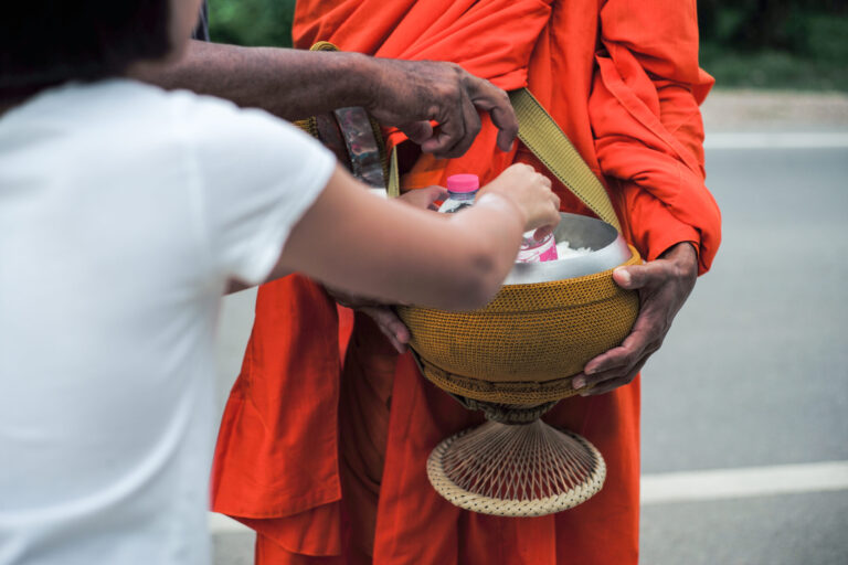 Rear view of girl puts the food into the bowl of monk during making the merit